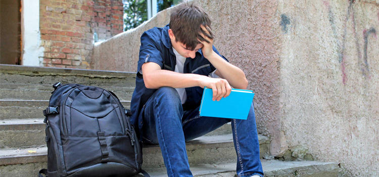 image of a distress teenagers seats on the floor holding his head